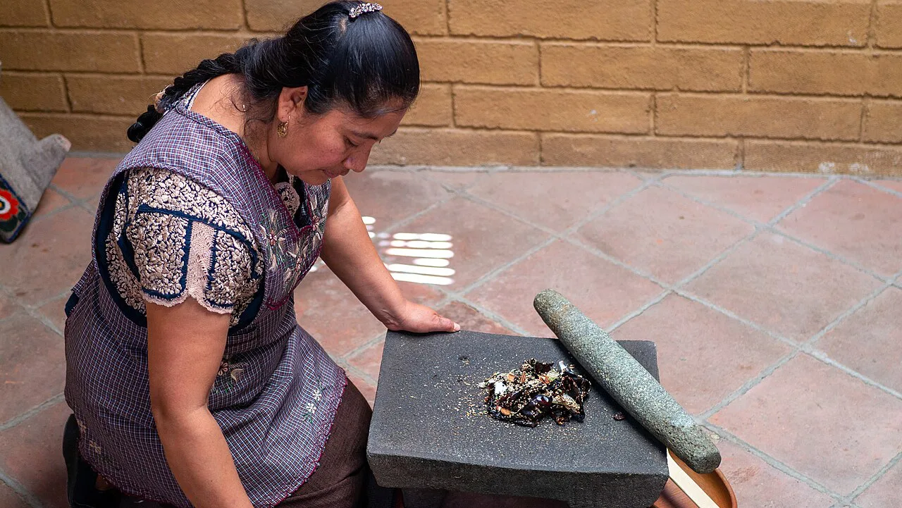 A woman grinding ingredients on a stone metate in Oaxaca.
